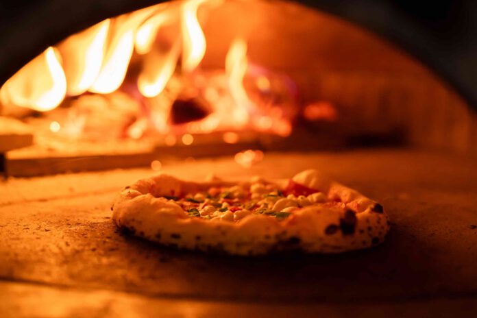 Pizza concept. Preparing traditional italian pizza. Long shovel for pizza, baking dough in a professional oven with open fire in interior of modern restaurant kitchen