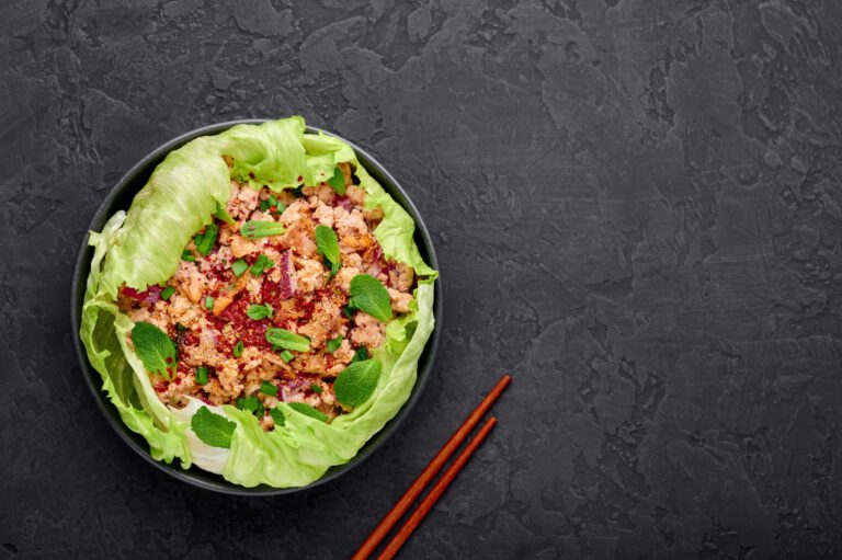 Laab Gai - Thai Minced Chicken Salad in black bowl at dark slate background. Larb is thailand cuisine dish with minced meat, fish sauce, lime juice, mint, lettuce and roasted rice. Thai Food.