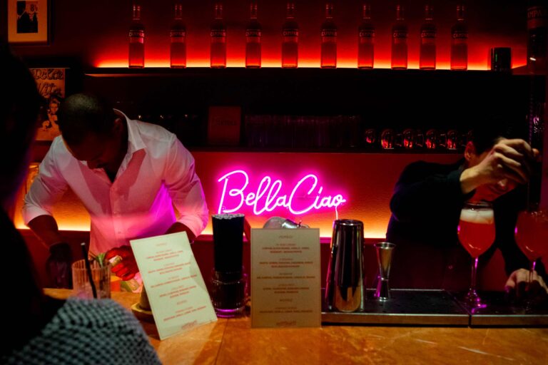 Bartenders at neon-lit bar mixing drinks.
