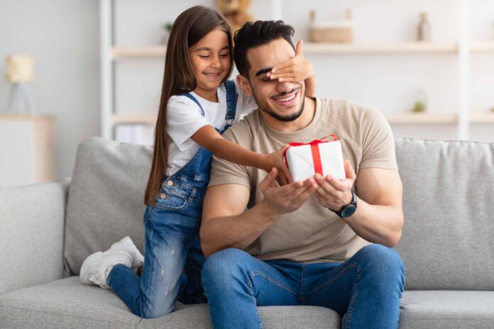 Child surprises dad with a gift on sofa.