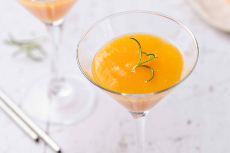 Mango cocktail in a glass with rosemary garnish.
