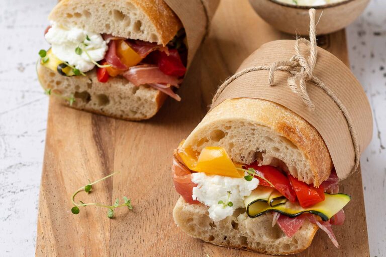 Gourmet sandwich with vegetables and cheese on board.