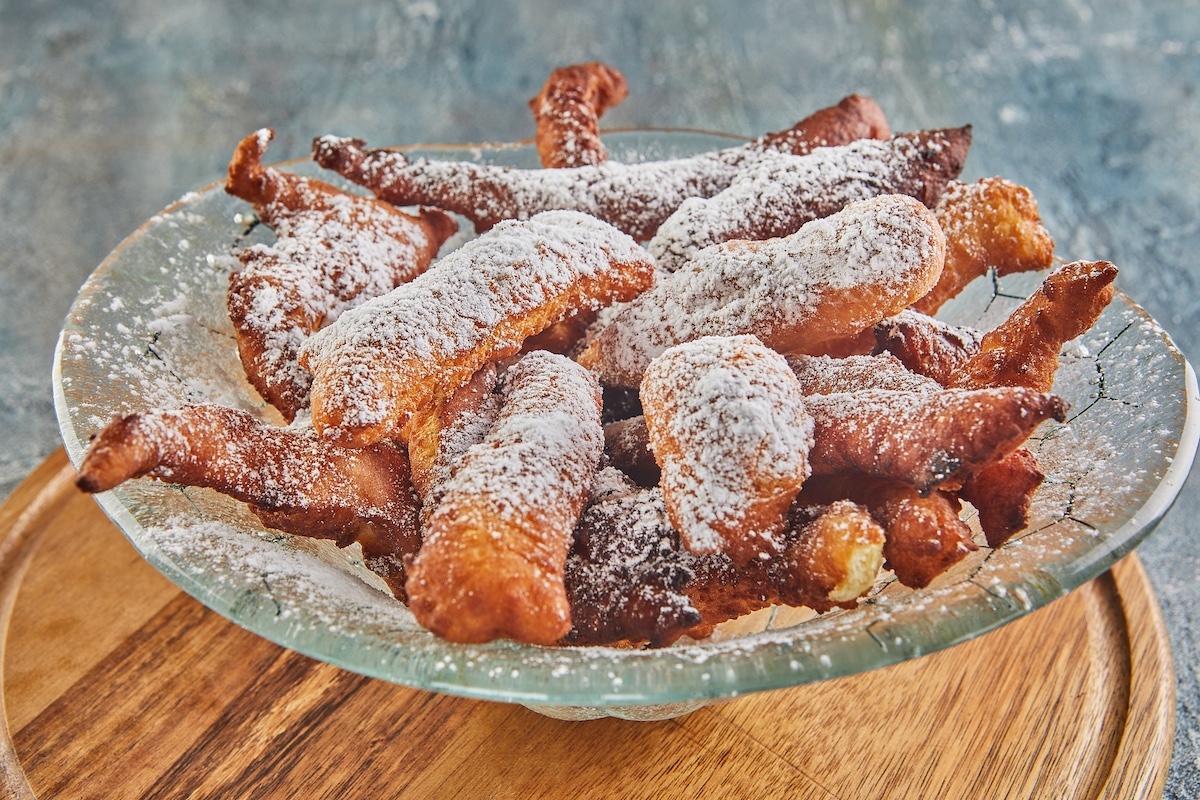bugnes, french donuts in transparent plate on wooden board