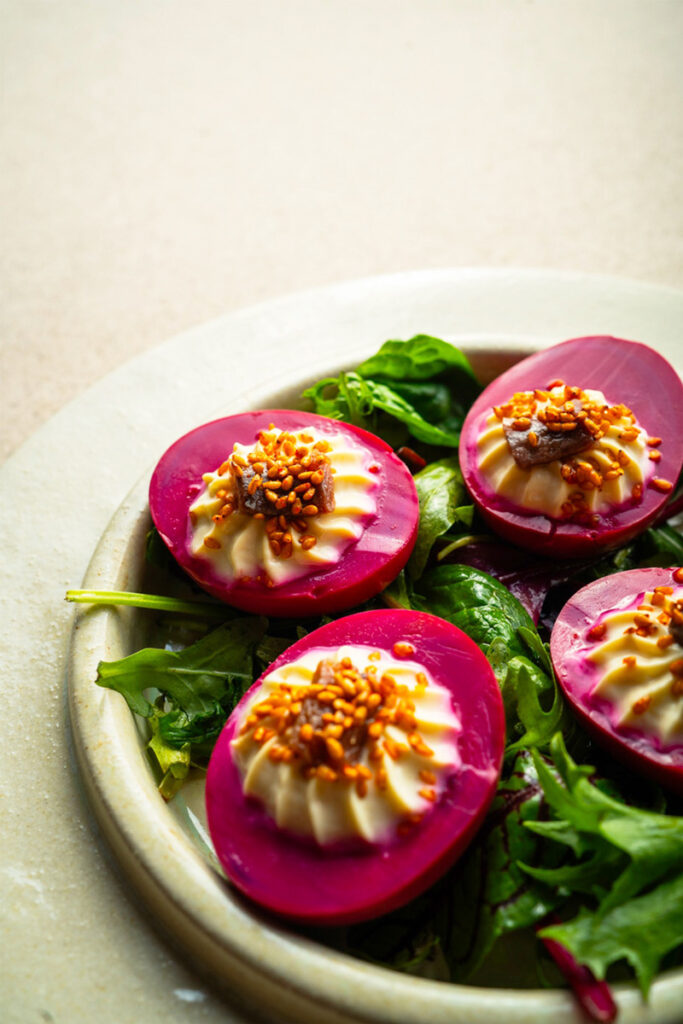 Beet deviled eggs on fresh salad greens.
