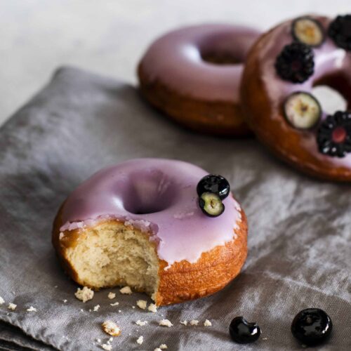 Purple glazed donuts with blackberries and blueberries.