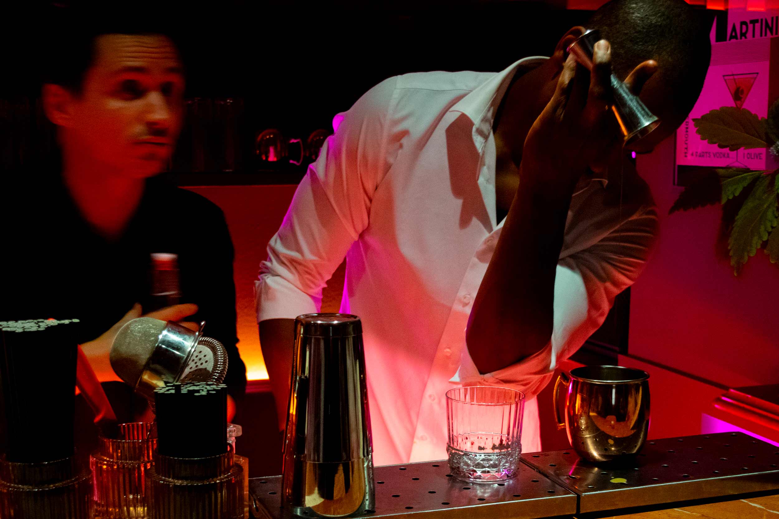 Two bartenders making cocktails in dim lighting.