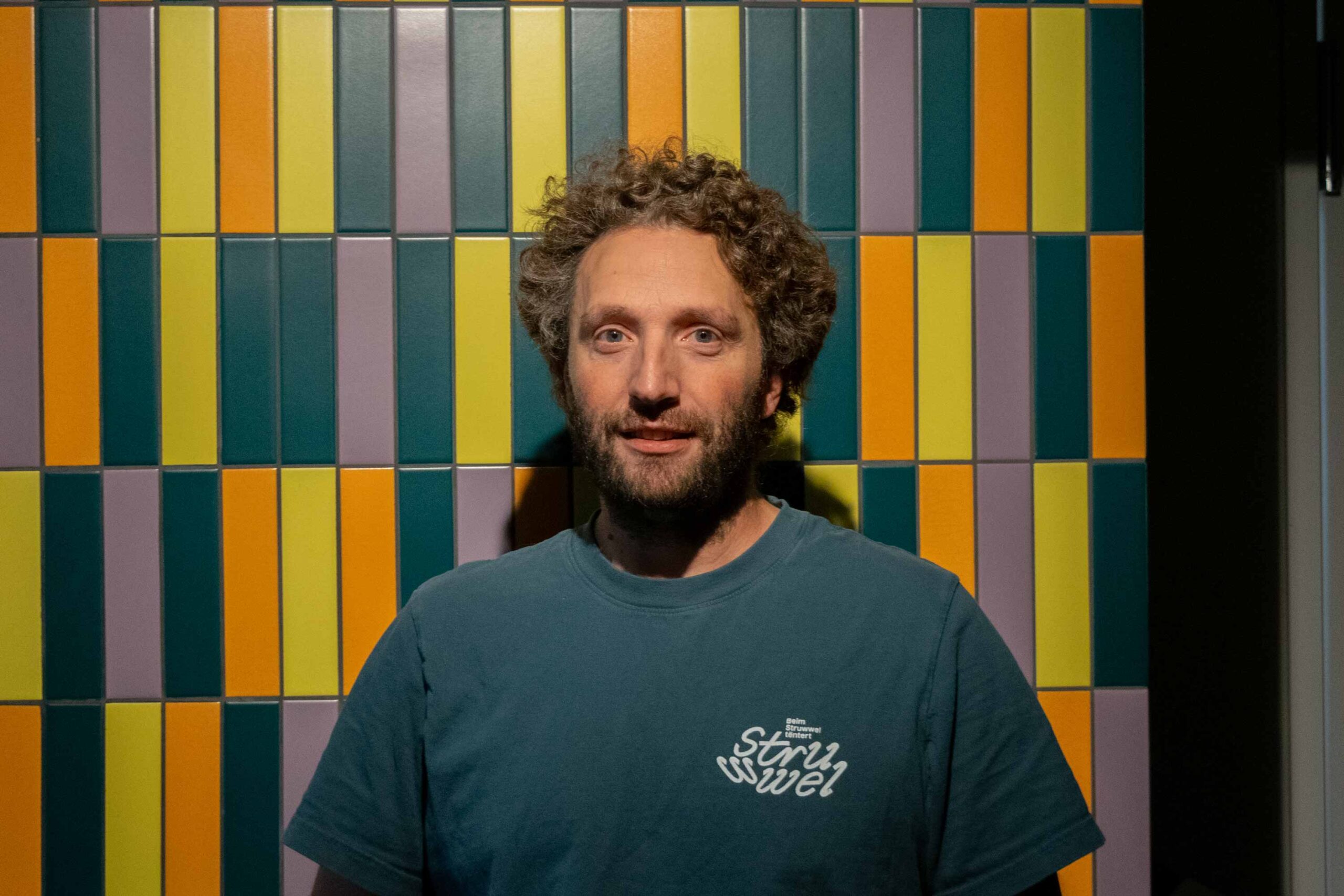 Person in front of colorful striped wall, smiling.