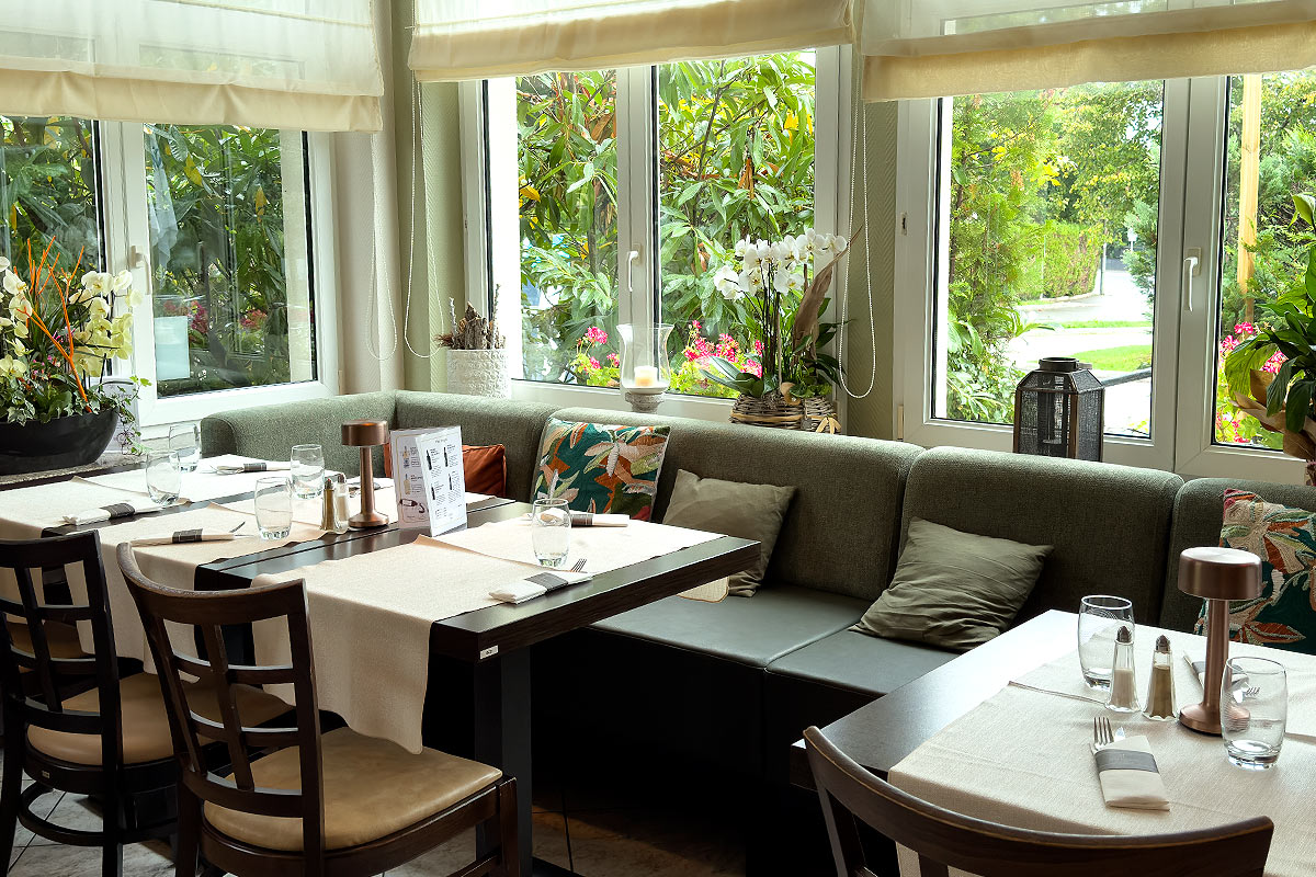 Cozy restaurant interior with large windows and plants.