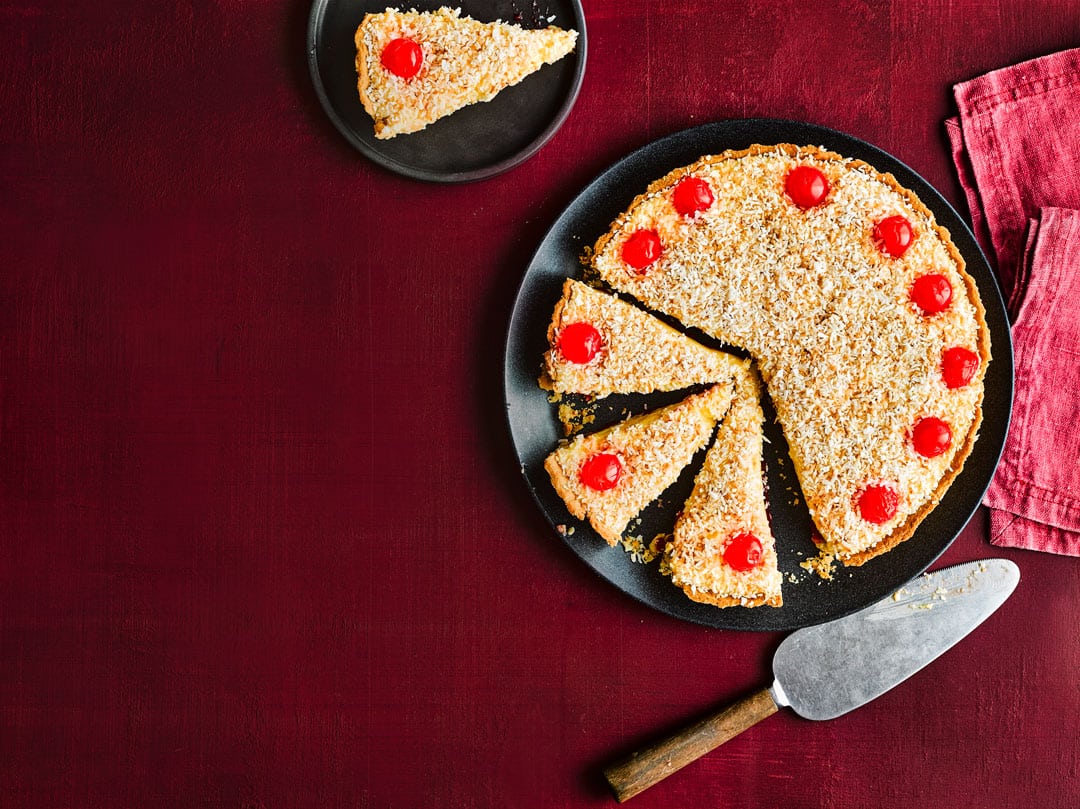 Coconut cherry tart on black plate with slicer.