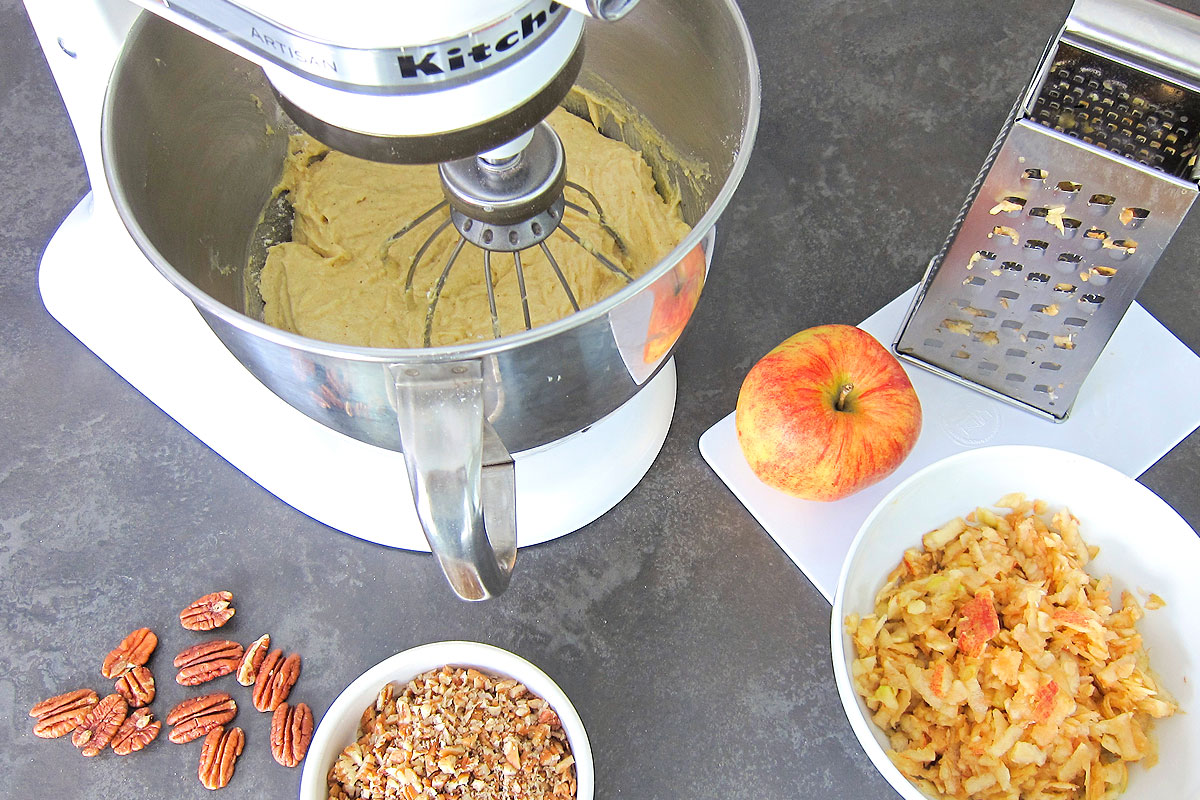 Mixer with apple cake ingredients: pecans, shredded apples.