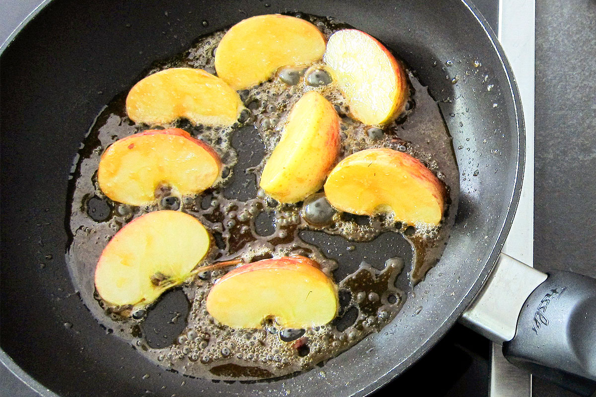 Sliced apples frying in butter in pan.