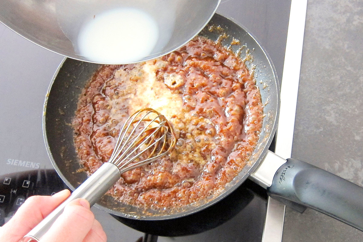 Whisking caramel sauce while adding milk in pan.