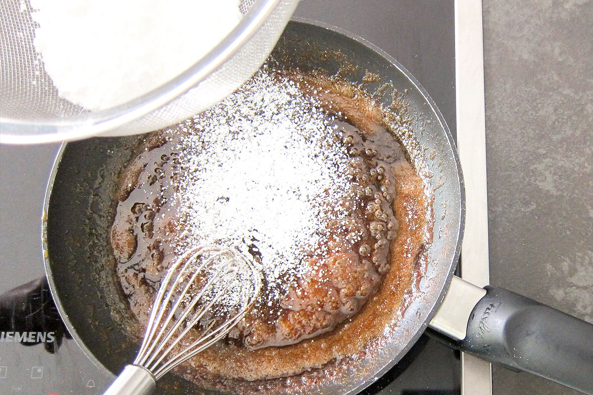 Whisking powdered sugar into caramel sauce on stove.